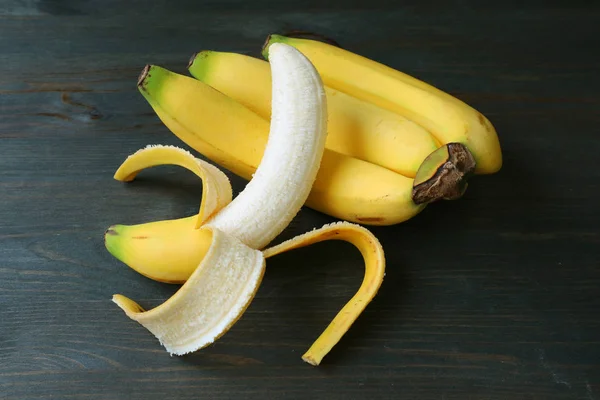 Peeled banana on a bunch of bananas isolated on dark color wooden background