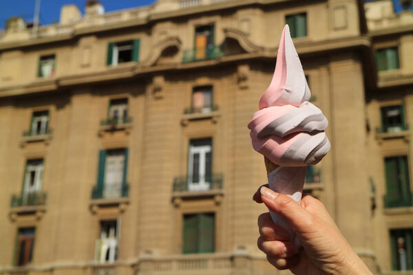 Woman Hand Holding Two tone Soft Serve Ice Cream Cone with Blurred Vintage Building in the Backdrop