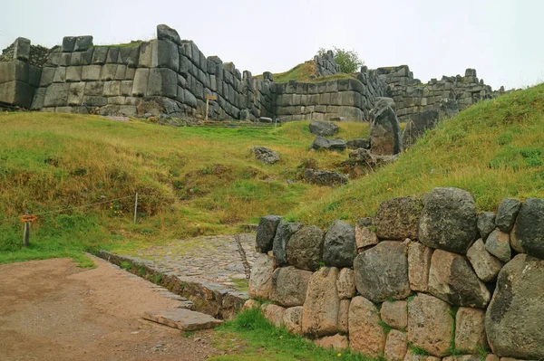 Stone paved way to the Sun Gate (INTIPUNKU written on the signpost) of Sacsayhuaman Incas citadel on the hilltop of Cusco, Peru
