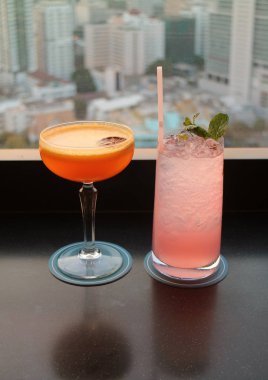 Çatıdaki barda arka planda bulanık şehir manzaralı iki bardak kokteyl.