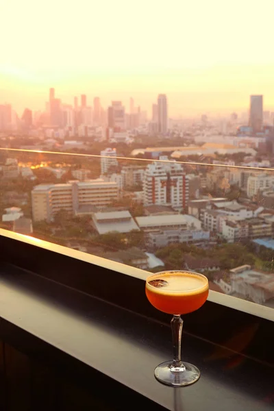 Glass of cocktail on the rooftop bar with aerial urban view in background