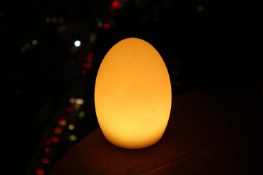 Yumurta şekilli lamba masanın üzerinde parlıyor ve fonda bokeh var.