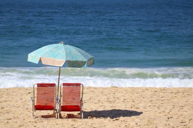 Copacabana sahilinde iki kırmızı plaj sandalyesi ve mavi şemsiye Atlantik Okyanusu 'ndan gelen çarpan dalgalara karşı, Rio de Janeiro, Brezilya