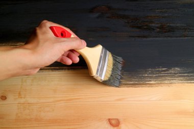 Adamın eli, fırça fırçasıyla ahşap tahtayı koyu gri boyayla boyuyor.