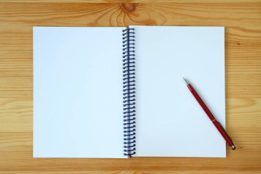 Açılmış bir defterin beyaz boş sayfası ve tahta arka planda kırmızı bir kalem.