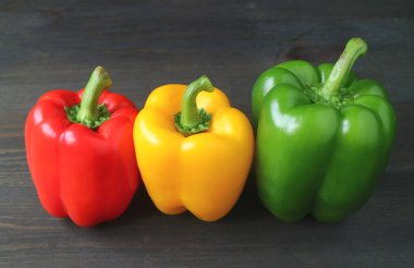 Siyah ahşap arka planda renkli olgun dolmalık biberler.