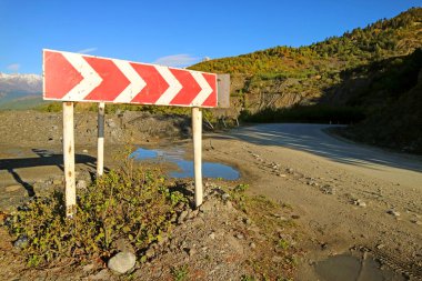 Boş dağ yolunda kırmızı ve beyaz çizgili tehlikeli tabela.