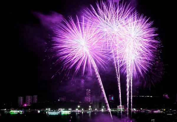 Vibrant pink and purple fireworks splashing in the night sky over the city