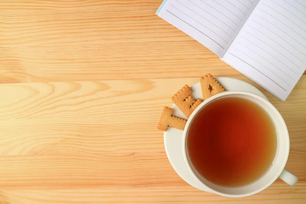 Top View of a Cup of Hot Tea and the Word TEA Made by Cookies, with a Lined Note Papers on Wooden Table