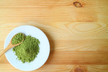 Tahta masa üzerinde bir çay kaşığı ile bir tabak kibrit yeşil çay tozu.