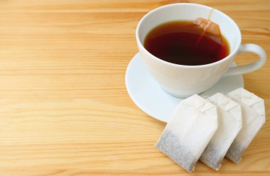 Çay poşetleri ve bir fincan taze demlenmiş sıcak çay ile ahşap masada servis edilen çay poşeti.