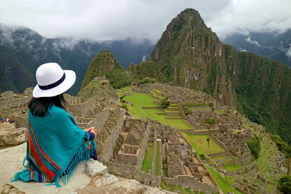 Uçurumda oturan Kadın Gezgin Machu Picchuin Cusco Bölgesi, Urubamba Eyaleti, Peru 'daki İnka harabelerine bakıyor.