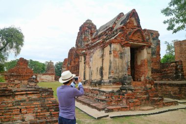 Turist, Tayland 'daki Ayutthaya Tarih Parkı' ndaki Wat Mahathat tapınağının etkileyici kalıntılarının fotoğraflarını çekiyor.