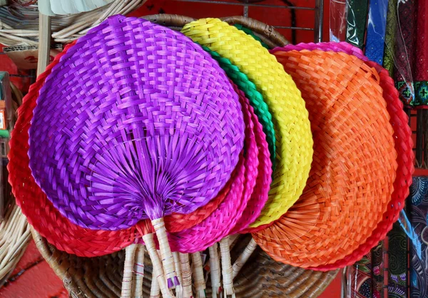 Colorful handmade natural raffia fans displayed in the shop at flea market in Thailand