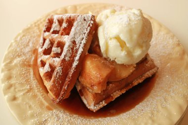 Bir tabak taze tarçınlı elmalı waffle Vanilyalı dondurma ve üzerine pudra şekeri serpiştirilmiş.