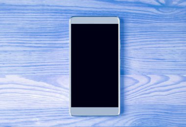 Mavi renkli ahşap masa üzerinde izole edilmiş gümüş bir akıllı telefonun üst görünümü metin ve tasarım için boş alanı var