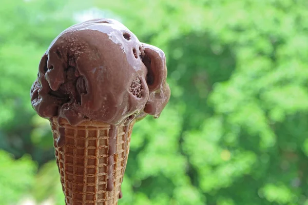 锥形圆锥中融化的巧克力冰淇淋与有复制空间的水泡绿色花园的对比 — 图库照片