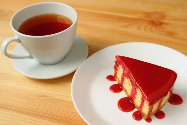 木製のテーブルで提供される熱いお茶のカップとラズベリーソースと焼きチーズケーキのプレート — ストック写真