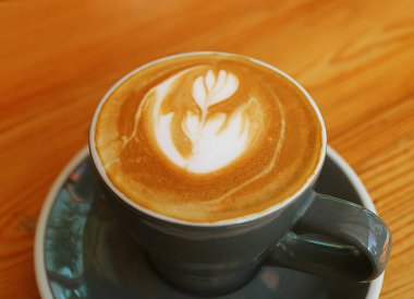 Tahta Masa 'da servis edilen koyu gri bir kupada Latte Art ile sıcak kapuçino kahvesi.
