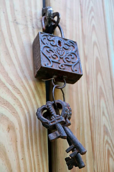 Vertical Photo of Dark Color Vintage Decorative Metal Keys and Lock on the Light Color Wooden Door