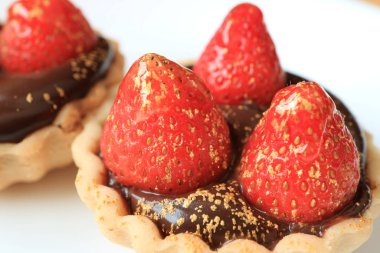 Üzerinde taze çilek ve beyaz tabakta servis edilen yenilebilir altın tozu olan çikolatalı tart.