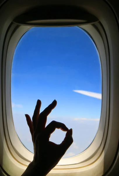 彼女の幸せな飛行中に鮮やかな青空と飛行機の翼と飛行機の窓に対してOkサインをポーズ女性の手のシルエット — ストック写真