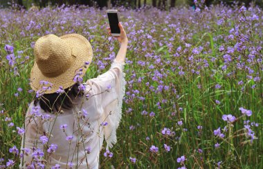 Genç bir kadın çiçek tarlasında cep telefonuyla selfie çekiyor.