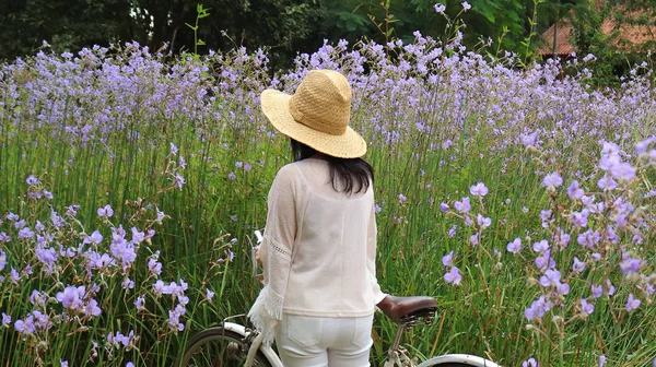 年轻女子骑着自行车站在美丽的紫罗兰花田里 — 图库照片