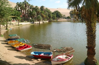 Güney Amerika, Ica, Peru 'daki Huacachina köyündeki vaha gölünün kıyısında renkli tekneler.