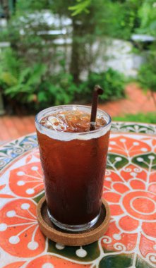 Arka planda bulanık tropik bahçesi olan bir bardak buzlu kahve.