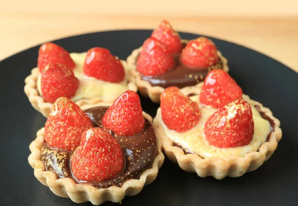 Fresh strawberry tarts with edible gold powder served on black plate