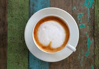 Renkli Kırsal Stil Ahşap Masa 'da Beyaz Kupa' da Kalp Şeklinde Latte Sanatı ile Sıcak Kahve, Seçici Odaklı Üst Görünüm