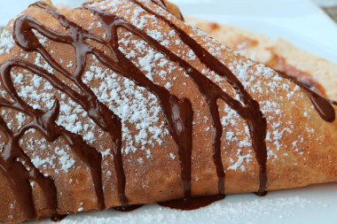 Kapalı Fransız usulü krep. Çikolata soslu ve buzlu şeker beyaz tabakta servis ediliyor.