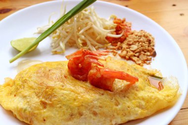 Beyaz tabakta servis edilen karidesli ev yapımı omlet sarılı Tayland eriştesi