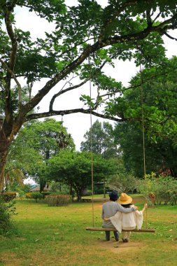 Bahçedeki ahşap salıncakta yan yana oturan bir çiftin dikey fotoğrafı