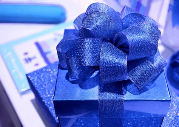 Closed up square shaped vibrant blue gift box with gritter blue ribbon bow, selective focus and blurred background
