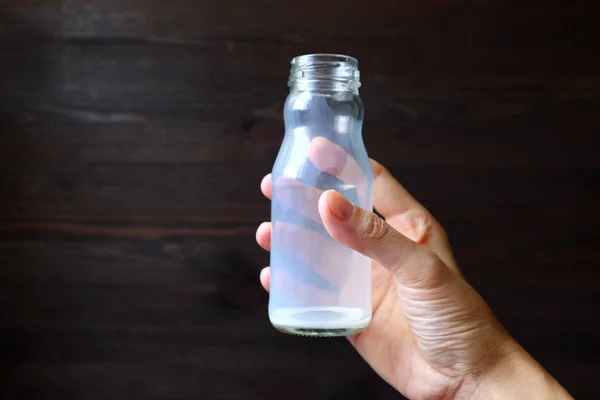 Empty glass bottle of milk in hand on dark brown wooden background