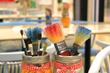 Arka planda bulanık resim sınıfıyla dolu kavanozlarda bir sürü boya fırçası var.