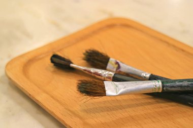 Masadaki tahta tepside üç boya fırçası.