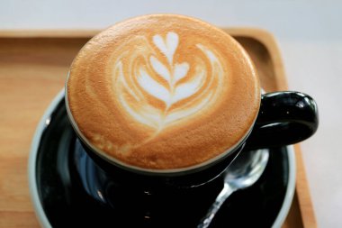 Bir fincan kapuçino ve ahşap tepside latte sanatı.