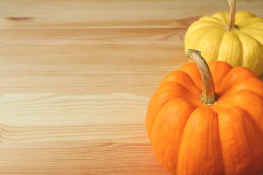 Açık kahverengi ahşap masa üzerinde sapı olan parlak sarı ve turuncu renkli olgun balkabakları tasarım ve metin için boş alanı var.