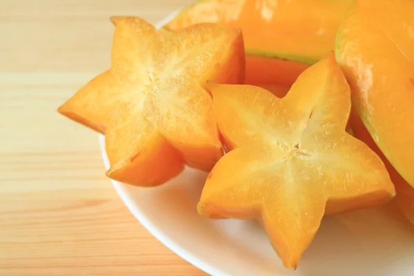 stock image Closed up pair of vibrant yellow sliced ripe Star Fruits on white plate served on wooden table