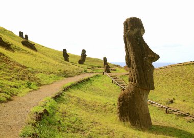 Rano Raraku Yanardağı 'nın yamacında terk edilmiş dev Moai heykelleri sürüsü arasında gezinti yolu, Paskalya Adası, Şili