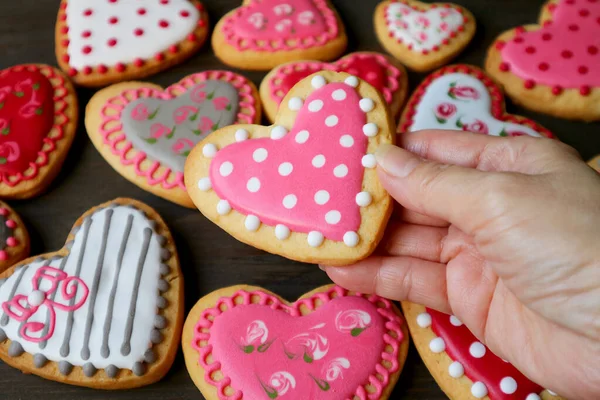 Closeup dotted heart shaped royal icing cookies in hand against heap of blurry colorful heart cookies