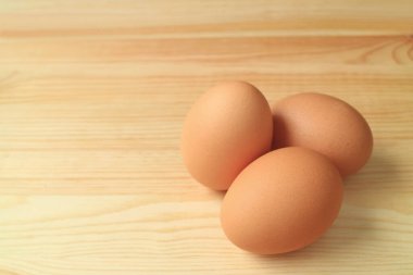 Ahşap masada izole edilmiş, yazı ve tasarım için boş yeri olan üç taze pişmemiş tavuk yumurtası.