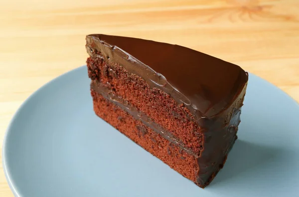 木製のテーブルの上にブループレート上で提供されるおいしいチョコレート層ケーキのピース — ストック写真