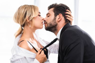 Ofiste flört ederken iş arkadaşı kravatını çeken seksi iş kadınının yan görünüşü