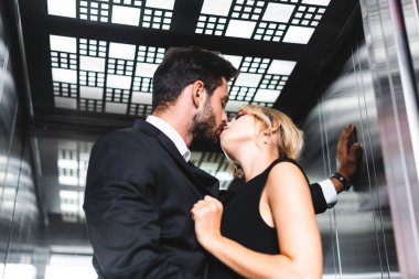 İş adamı ofis asansöründe iş arkadaşını öpüyor.
