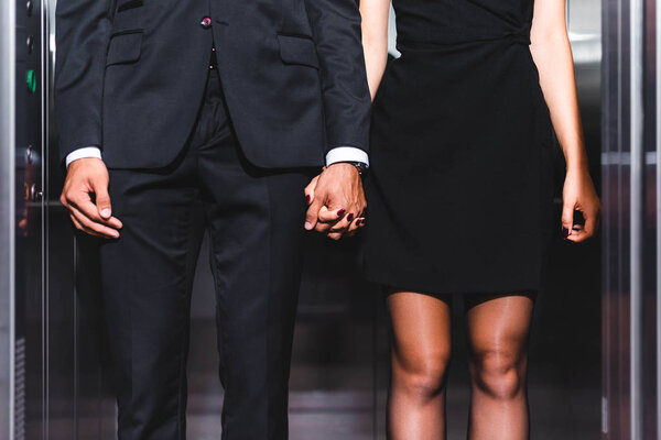 Cropped view of business couple holding hands in office elevator 