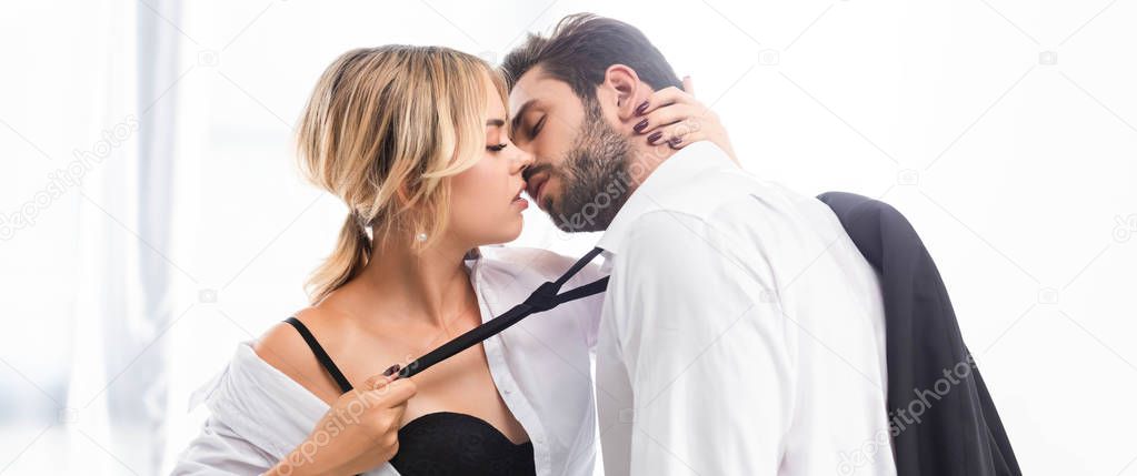 Sexy woman pulling businessman tie while flirting in office, panoramic shot
